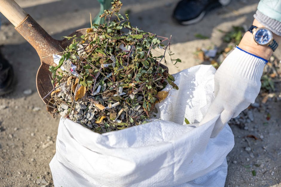 A pile of mixed waste materials and cardboard boxes rests against a weathered concrete block wall outdoors. The debris includes flattened cardboard boxes, some with printed labels and logos, as well a